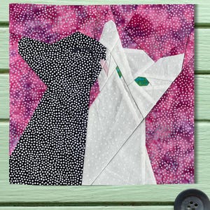 May include: A paper pieced quilt block featuring a black and white dog and a white cat on a pink background with white polka dots.
