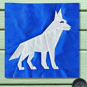 May include: A white origami dog stands on a blue background. The dog is made of folded paper, with sharp angles and clean lines. The background is a solid, deep blue, creating a striking contrast. The artwork is square and appears to be a paper craft.