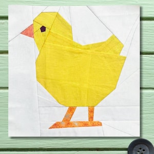 May include: A geometric quilt block featuring a yellow chick with an orange beak and feet. The chick is set against a white background with angled lines, creating a modern, patchwork design. The chick's eye is a small purple square.