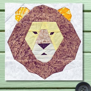 May include: A fabric lion face, constructed from various patterned and solid fabrics. The lion features a yellow face, brown mane with purple accents, and yellow ears. The design is geometric and appears to be part of a quilt block.