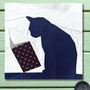 Puede incluir: Una pieza de arte textil que presenta una silueta de gato estilizada en azul marino, blanco y tela estampada. El gato se representa sentado, con formas geométricas que crean su forma. El fondo es una superficie de madera verde claro. Una obra de arte textil única.