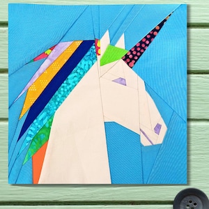 May include: A colorful, geometric unicorn design on a square, light blue background. The unicorn's head is white, with a horn featuring a pink and black polka dot pattern. Its mane is a vibrant mix of rainbow colors, including yellow, blue, and green.