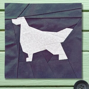 Op de afbeelding: Een vierkant stoffen kunstwerk met een wit honden silhouet tegen een donkerblauwe achtergrond. De hond is gemaakt van witte stof met een subtiel patroon. De achtergrond is een patchwork ontwerp van donkerblauwe stof.