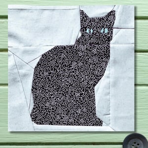Könnte beinhalten: Ein quadratisches Stoffstück mit einer schwarzen Katzen-Silhouette mit einem weißen, geschwungenen Muster. Die Katze hat hellblaue Augen und ist vor einem weißen und grauen Hintergrund platziert. Es ist wahrscheinlich Teil eines Quilt- oder Textilprojekts.