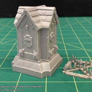May include: A gray plastic model of a gothic tomb with a skull and crossbones on the front. The tomb is on a base with a cracked surface. A separate gray plastic model of a spiked trap is also shown. The trap has the words "REMOVE BEFORE CASTING" printed on it.