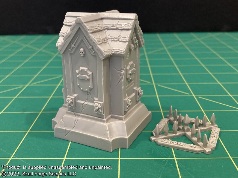 May include: A gray plastic model of a gothic tomb with a skull and crossbones on the front. The tomb is on a base with a cracked surface. A separate gray plastic model of a spiked trap is also shown. The trap has the words "REMOVE BEFORE CASTING" printed on it.