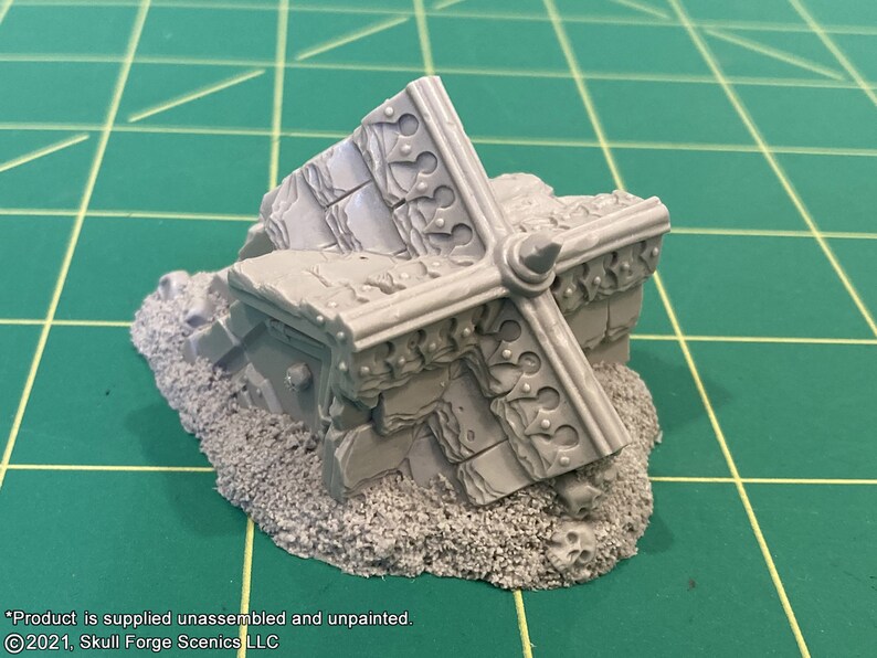 K&ouml;nnte beinhalten: Ein detailliertes, graues Plastikmodell einer zerst&ouml;rten Steinstruktur mit einem dekorativen, kreuzf&ouml;rmigen Design. Das Modell steht auf einem Bett aus grauem, strukturiertem Sand.