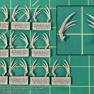 May include: A set of 12 miniature plastic claws, each with three points, for use in model building and miniature gaming. The claws are arranged in rows of three, with each row labeled with the text "2024 SKULL FORGE SCENICS".