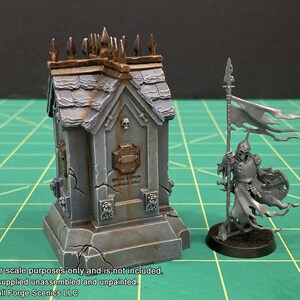 May include: A gray, weathered, miniature stone mausoleum with a skull and crossbones design. The mausoleum is on a base with a cracked surface. A miniature skeletal figure with a tattered flag is standing next to the mausoleum.