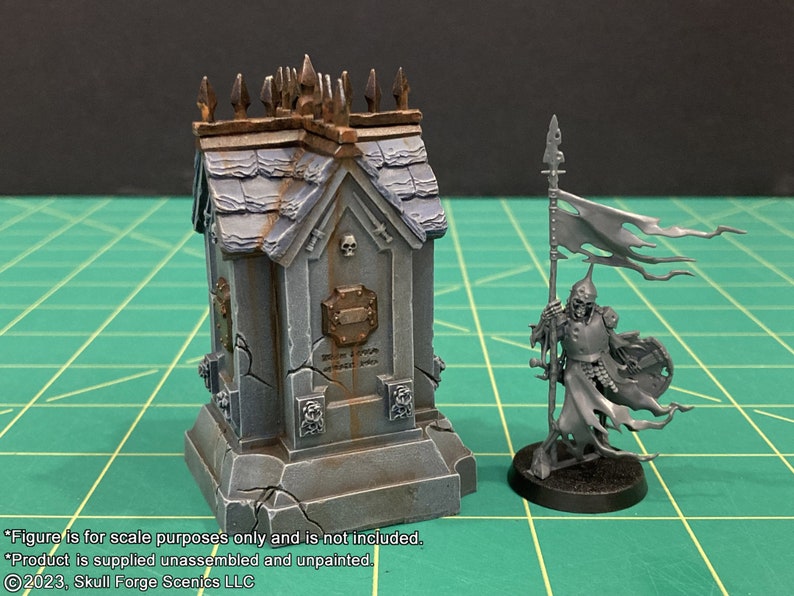 May include: A gray, weathered, miniature stone mausoleum with a skull and crossbones design. The mausoleum is on a base with a cracked surface. A miniature skeletal figure with a tattered flag is standing next to the mausoleum.