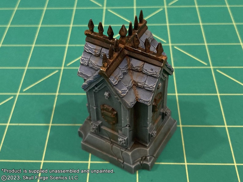 May include: A small, gray stone mausoleum with a weathered, slate roof and a decorative iron fence. The mausoleum has a small, rectangular plaque on the front.