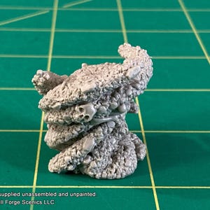 May include: A grey, unpainted miniature terrain piece with a textured, organic appearance. The piece features several small skulls and a twisted, layered design, suitable for tabletop gaming. The product is supplied unassembled.