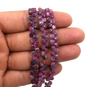 May include: A strand of pink ruby gemstone beads, faceted and round, with a slightly irregular shape. The beads are strung on a clear thread and are approximately 4mm in diameter.