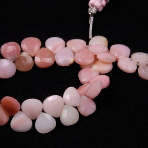 May include: A strand of pink opal gemstone beads in a heart shape. The beads are faceted and have a translucent appearance.