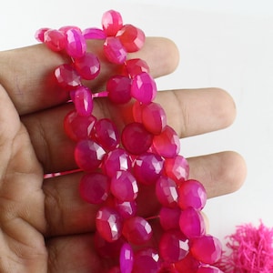 Könnte beinhalten: Eine Strähne aus rosafarbenen Chalcedon-Edelsteinkugeln. Die Kugeln sind facettiert und haben eine glatte, polierte Oberfläche. Die Kugeln sind auf einer durchsichtigen Gummikordel aufgefädelt.