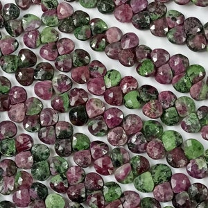 Pode incluir: Um fio de contas de pedras preciosas facetadas verdes e rosadas. As contas são de forma oval e têm um acabamento liso e polido.