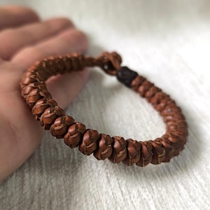 Può includere: Bracciale in pelle marrone intrecciata. Il bracciale è composto da piccoli pezzi di pelle fittamente intrecciati, creando un aspetto strutturato. Il bracciale è di colore marrone caldo e ha un design semplice e rustico. Circonferenza di circa 18 cm.