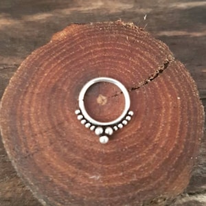 Puede incluir: Un anillo de plata con una fila de pequeñas cuentas alrededor de la parte superior y una cuenta más grande en el centro.