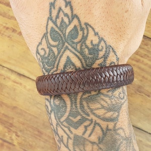 Puede incluir: Un brazalete trenzado de cuero marr&oacute;n en la mu&ntilde;eca de una persona.