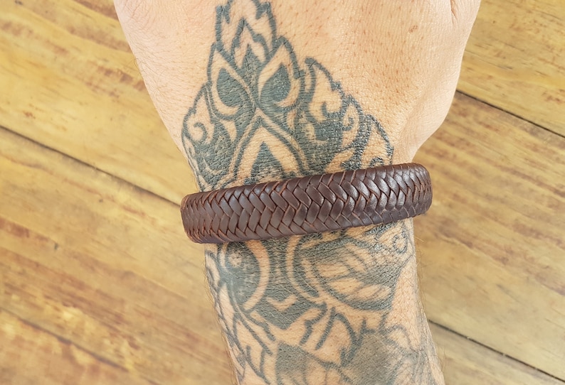 Puede incluir: Un brazalete trenzado de cuero marr&oacute;n en la mu&ntilde;eca de una persona.