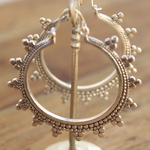 May include: Silver hoop earrings with a textured, beaded design. The earrings are displayed on a stand.