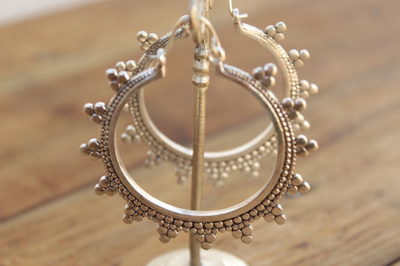 May include: Silver hoop earrings with a textured, beaded design. The earrings are displayed on a stand.