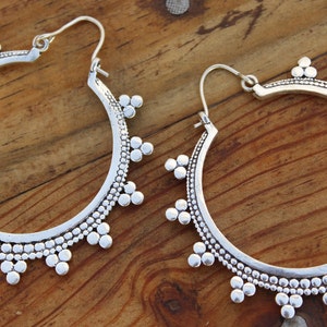 May include: A pair of silver hoop earrings with a beaded design. The earrings are large and have a circular shape.