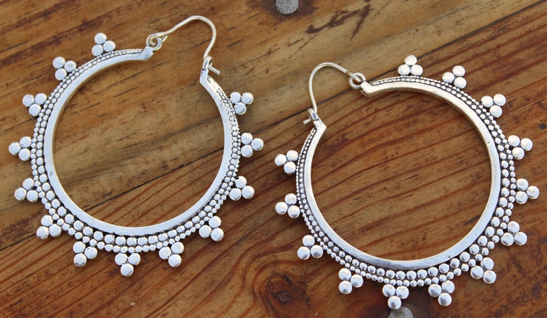 May include: A pair of silver hoop earrings with a beaded design. The earrings are large and have a circular shape.