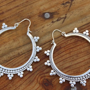 May include: A pair of silver hoop earrings with a beaded design. The earrings have a circular shape and are decorated with small, round beads.