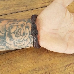 Puede incluir: Un brazalete de cuero marr&oacute;n con un dise&ntilde;o trenzado. El brazalete est&aacute; atado con un nudo.