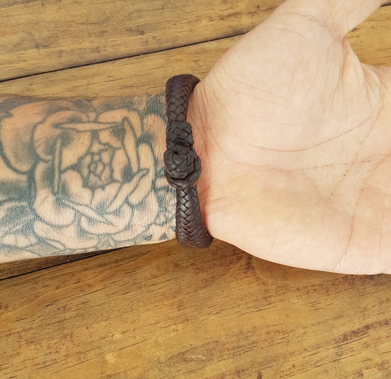 Puede incluir: Un brazalete de cuero marr&oacute;n con un dise&ntilde;o trenzado. El brazalete est&aacute; atado con un nudo.