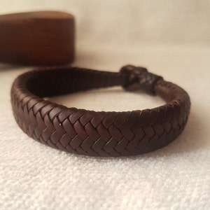 Puede incluir: Un brazalete trenzado de cuero marr&oacute;n con un dise&ntilde;o tejido.