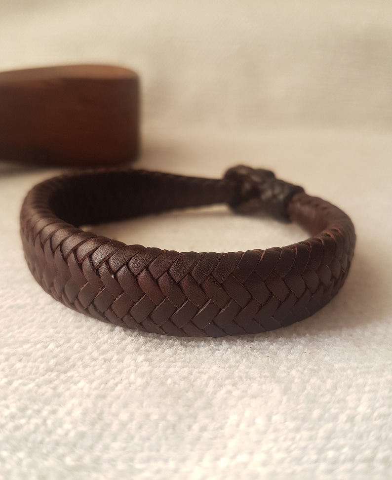 Puede incluir: Un brazalete trenzado de cuero marr&oacute;n con un dise&ntilde;o tejido.