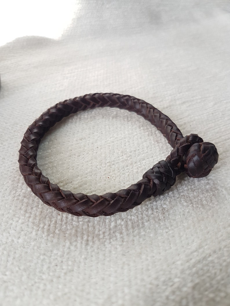 Puede incluir: Un brazalete trenzado de cuero marr&oacute;n con cierre anudado.