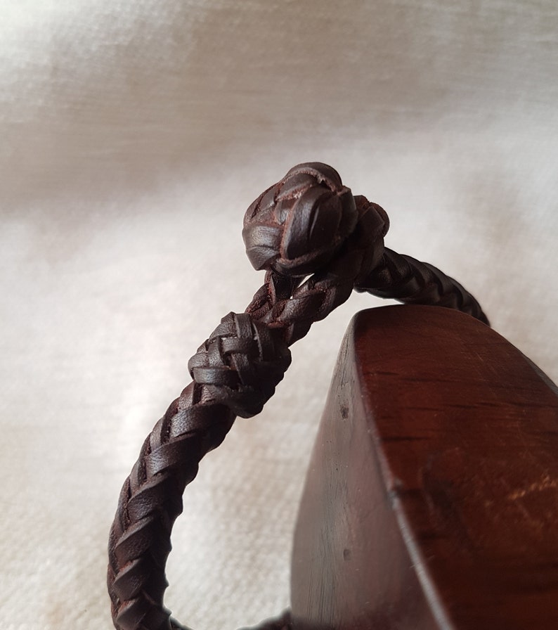 Puede incluir: Primer plano de una pulsera de cuero marr&oacute;n con un nudo trenzado. La pulsera est&aacute; hecha de cuero grueso y tejido y tiene un dise&ntilde;o simple y elegante.
