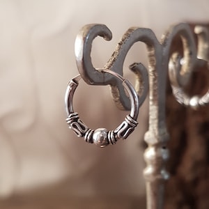 May include: Silver hoop earrings with a decorative design and a small bead accent.
