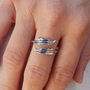 Op de afbeelding: Een zilveren ring met twee verenontwerpen. De ring is verstelbaar en kan aan elke vinger worden gedragen.