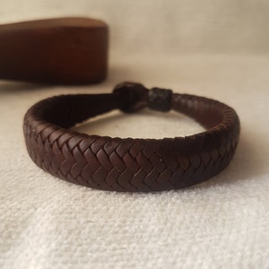 Puede incluir: Un brazalete de cuero marr&oacute;n con un dise&ntilde;o trenzado.