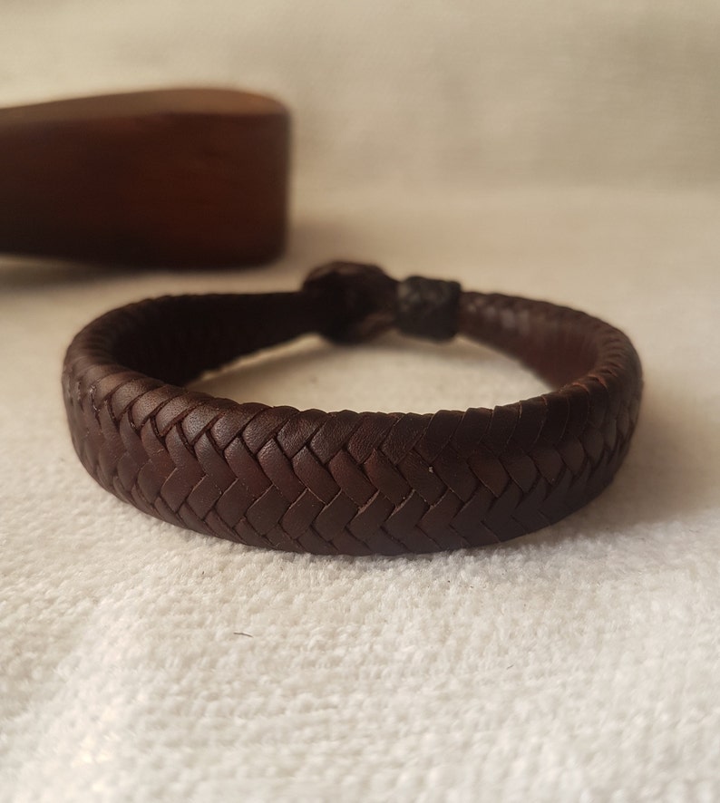 Puede incluir: Un brazalete de cuero marr&oacute;n con un dise&ntilde;o trenzado.