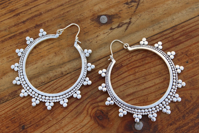 May include: A pair of silver hoop earrings with a beaded design. The earrings are large and have a circular shape.