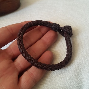 Puede incluir: Un brazalete de cuero marr&oacute;n con un dise&ntilde;o trenzado. El brazalete est&aacute; atado con un nudo.