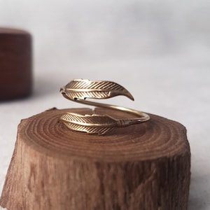 May include: A gold-toned ring with a double feather design. The ring is adjustable and can be worn on any finger.