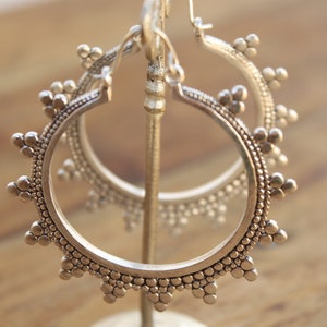 May include: A pair of silver hoop earrings with a beaded design. The earrings are displayed on a stand.