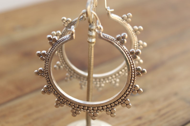 May include: A pair of silver hoop earrings with a beaded design. The earrings are displayed on a stand.