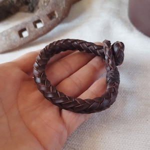 Peut inclure: Un bracelet en cuir marron tressé avec une fermeture nouée.