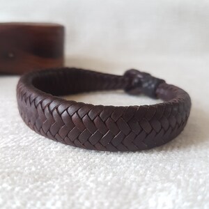Puede incluir: Un brazalete de cuero marr&oacute;n oscuro con un dise&ntilde;o trenzado.