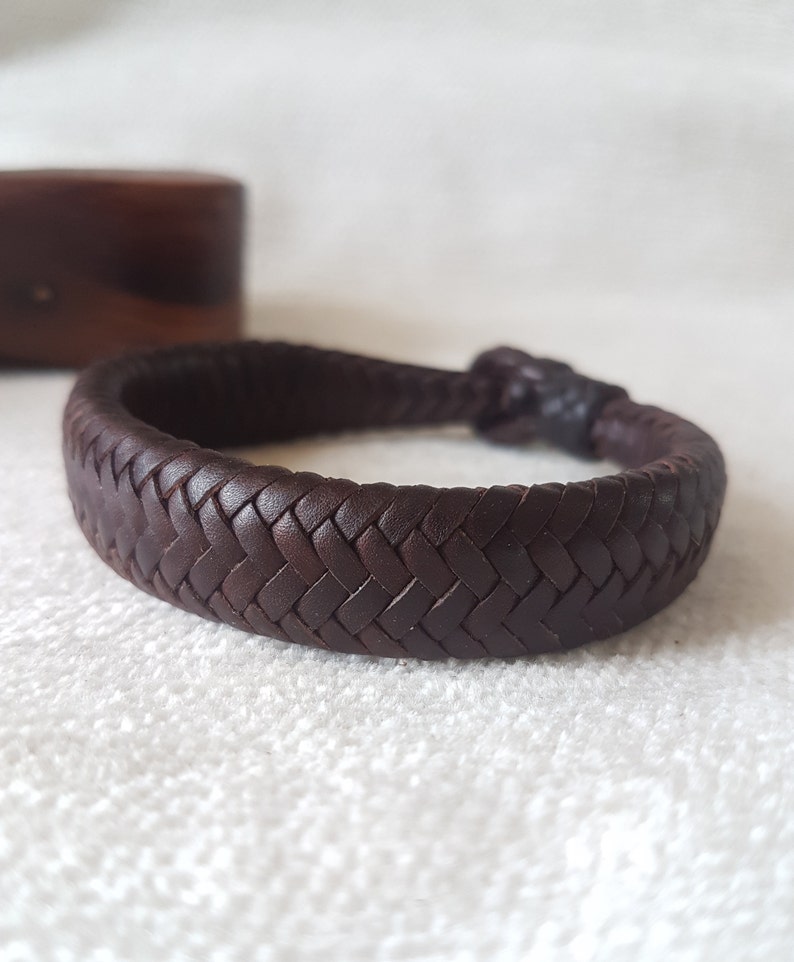 Puede incluir: Un brazalete de cuero marr&oacute;n oscuro con un dise&ntilde;o trenzado.