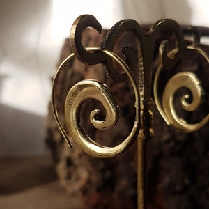 Puede incluir: Un par de pendientes de aro de oro con un diseño en espiral. Los pendientes se muestran en un soporte decorativo.