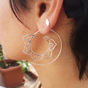 May include: Silver hoop earrings featuring a delicate mandala design. The earrings are large and circular in shape.