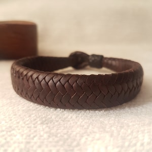 Puede incluir: Un brazalete de cuero marr&oacute;n con un dise&ntilde;o trenzado.